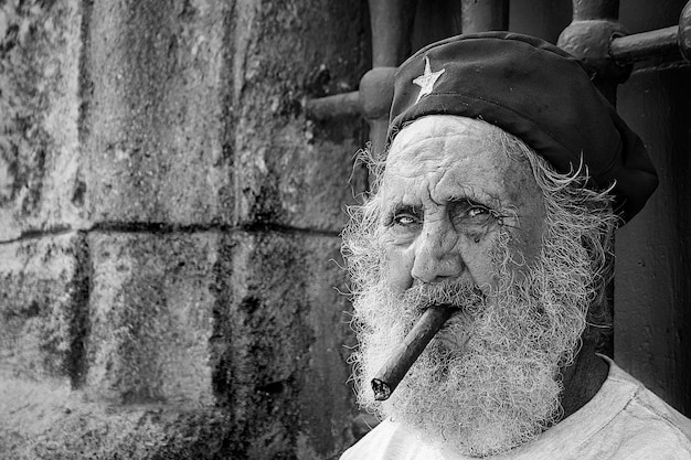 Old man with a beard and his beret smokes a cigar on a street in old havana