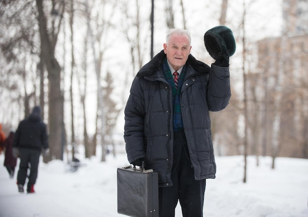 An old man with case takes off his hat outdoors