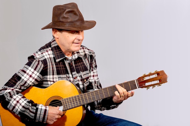 Old man with light eyes playing guitar with gaucho hat