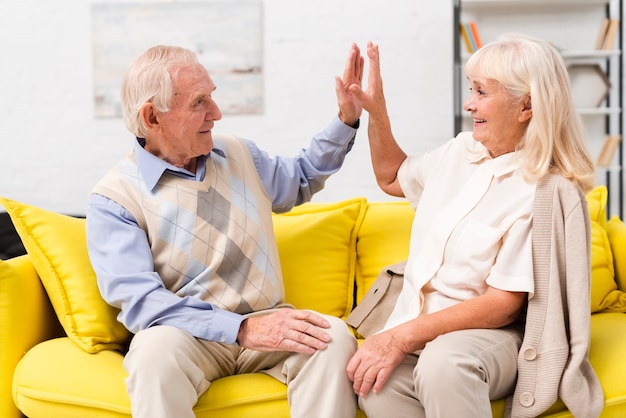 Photo old man and woman high fiving on yellow sofa