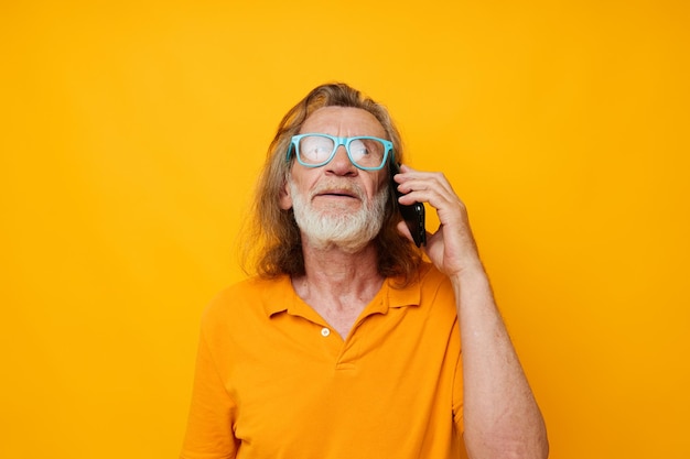 Old man in yellow Tshirts and glasses talking on the phone isolated background