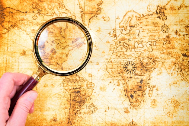 Old map and magnifying glass in a hand explored it. Vintage travel background