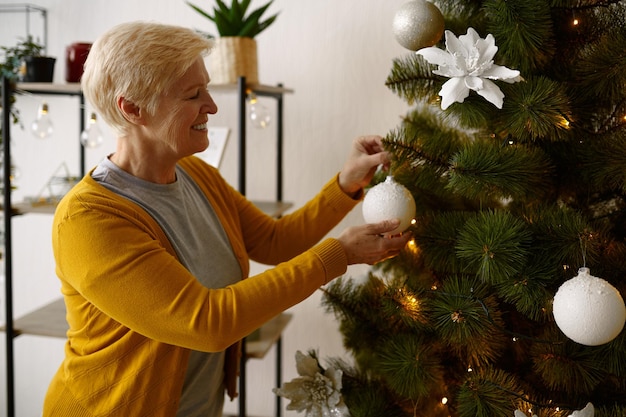 Vecchia donna matura che appende la decorazione dell'ornamento della palla dell'albero di natale. festa di natale e capodanno