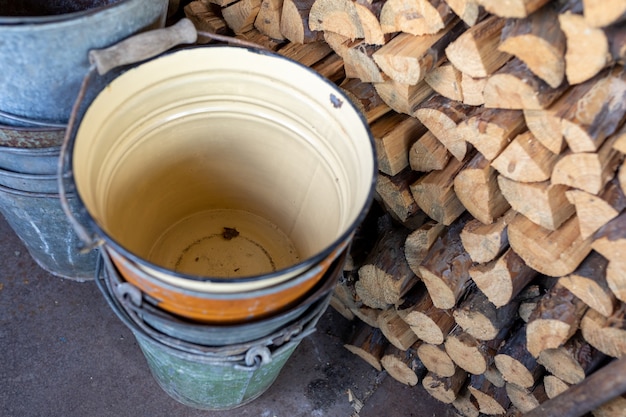 Vecchi secchi di metallo si trovano nel capannone vicino a una catasta di legna da ardere tagliata
