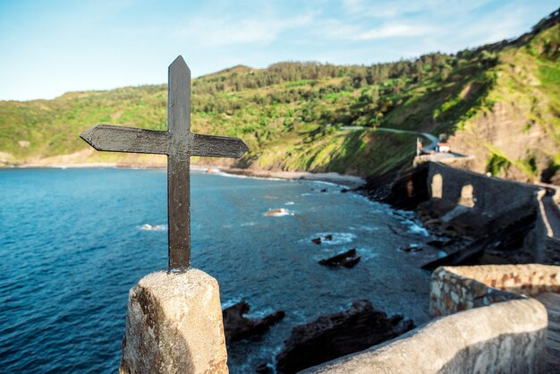 바위 해안선과 바다의 배경에 San Juan de Gaztelugatxe 섬의 울타리에 오래된 금속 교회 십자가