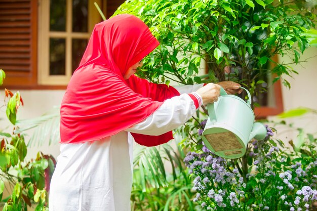 Old muslim woman watering flowers at backyard