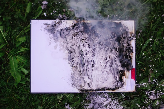 Old notepad burning on green summer grass outdoors.