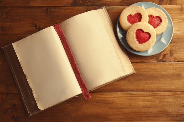 Photo old open book and biscuits on wooden table top view