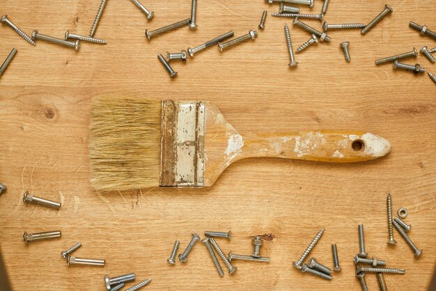 An old paint brush and screws on a wooden table. Home design banner.