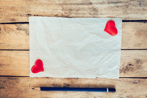 Vecchia carta e cuore rosso con matita su sfondo di legno per biglietto di auguri di san valentino.