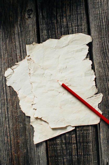 Old paper sheet on old wooden wall, lying next to a red pencil