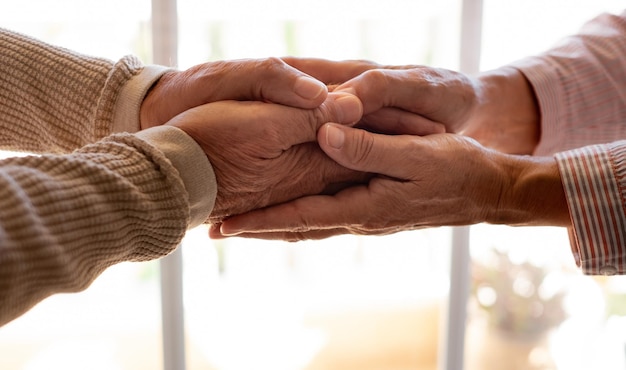 Пожилые люди, взявшись за руки крупным планом, смотрят на пожилую семейную пару на пенсии, выражающую заботу и поддержку