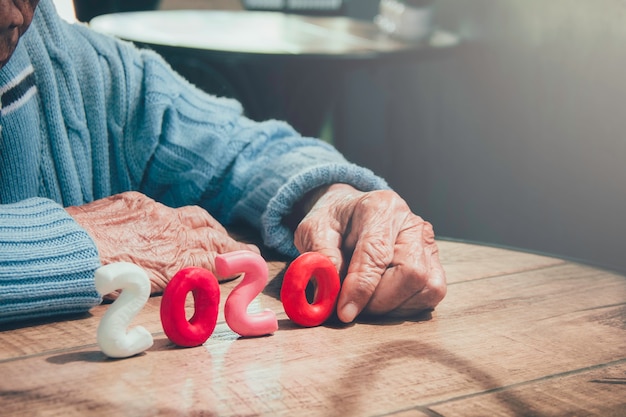 古い人の手が木製のテーブルに番号2020を保持しています。コンセプト：2020年の世界の高齢人口は劇的に増加します。