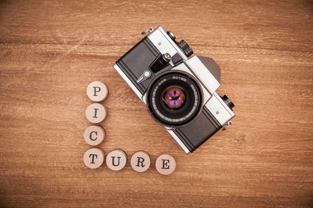 Old photo camera with lens on wooden table.