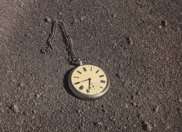 An old pocket watch lies on dry ground. Past and future tense.