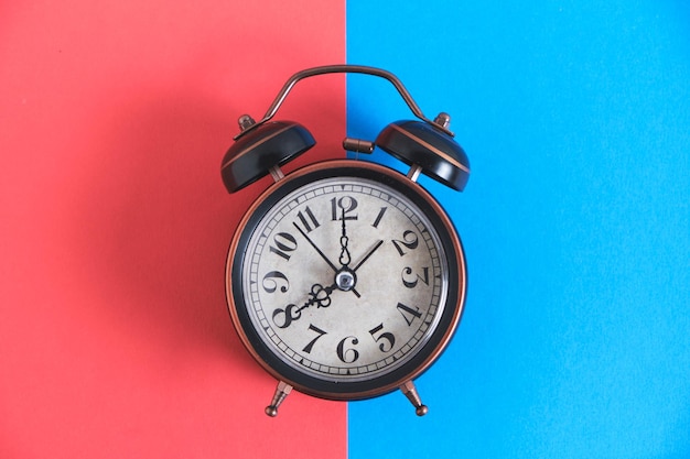 Old retro alarm clock on red and blue background.