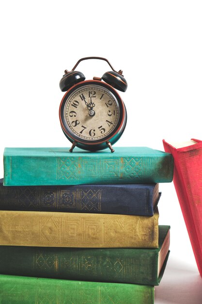 흰색 바탕에 빈티지 책 더미에 오래 된 복고풍 알람 시계.