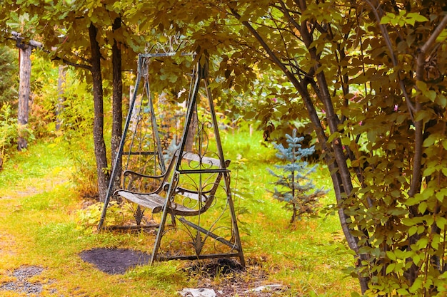 An old retro iron wrought metal swing with a wooden bench in a vintage style stands in a garden