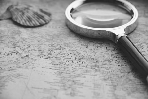 Old retro map of world is pressed with shells and magnifying\
glass.vacation, recreation, and travel in a black and white\
photo.