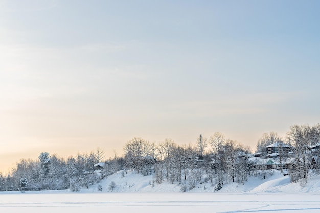 雪に覆われた湖のほとりにある古いロシアの村の家と冬の木々