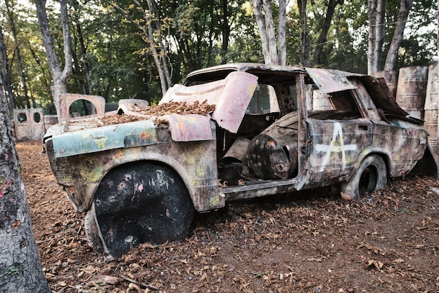 An old rusty and abandoned car at a paintball base behind which players excited by the game are hiding