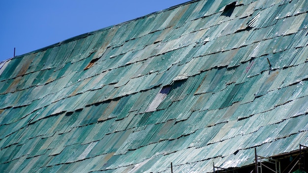 Old rusty green metal roof with a blue sky in the background long time zinc roof run to rust