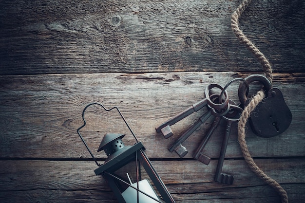 Old rusty lock with keys vintage lamp and rope on wooden board Top view