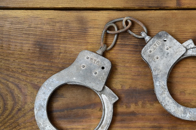 Old and rusty police handcuffs lie on a scratched wooden surface