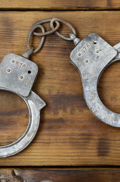 Old and rusty police handcuffs lie on a scratched wooden surface.