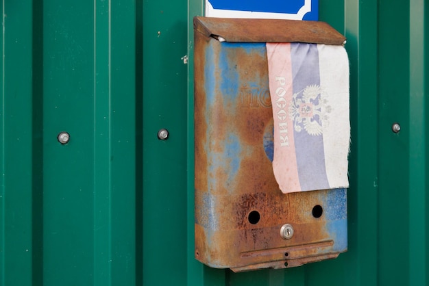 Photo old rusty russian mailbox on the wall with faded small fabric russian flag with with coat of arms