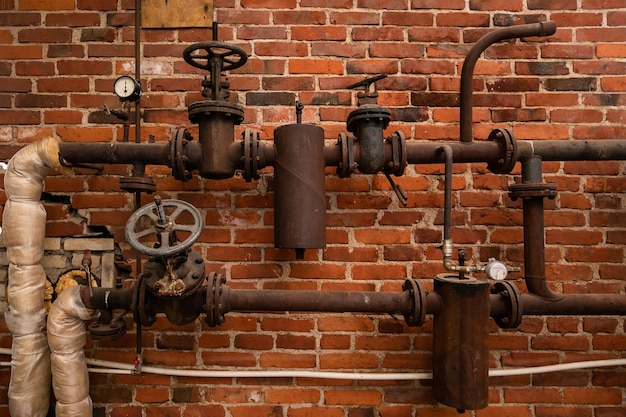 Old rusty water pipes with shutoff valves and sensors in an industrial building on a brick wall