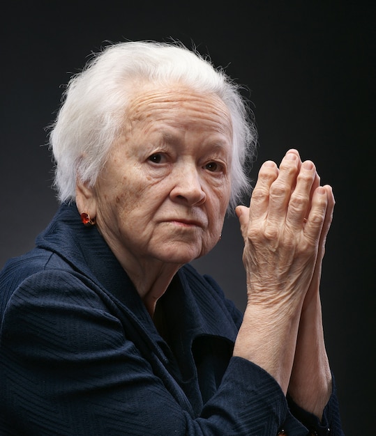 Old sad woman posing in studio over gray background