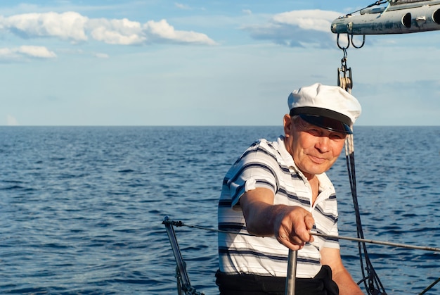 Старый моряк на своей парусной лодке на фоне морского пейзажа
