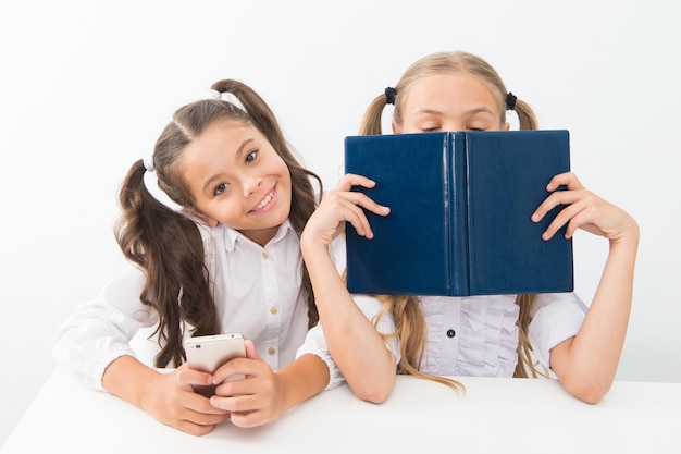 Old school against modern Schoolgirl hold mobile phone modern smartphone while her friend enjoy old book as analog data storage Technology against experience New generation educational demands