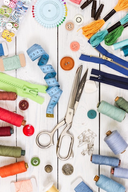 Old scissors buttons threads measuring tape and sewing supplies on light wooden background top view