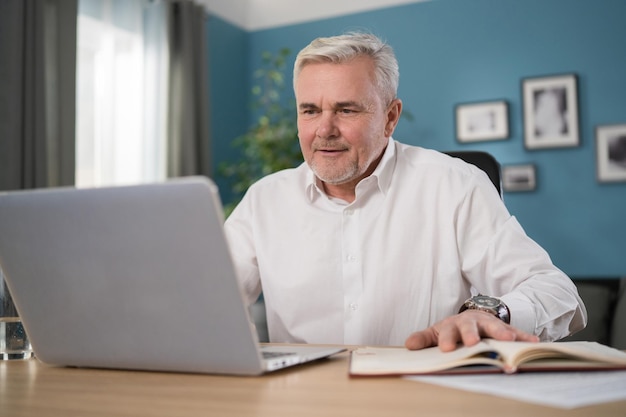 Старый пожилой мужчина проверяет домашние финансы и счета, он рассчитывает расходы с помощью компьютера и пишет