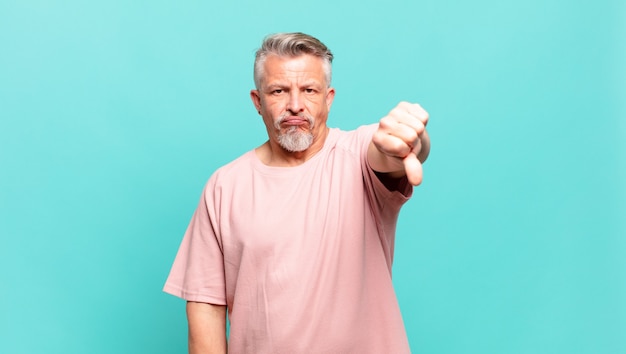 Old senior man feeling cross, angry, annoyed, disappointed or displeased, showing thumbs down with a serious look