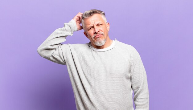 Old senior man feeling puzzled and confused, scratching head and looking to the side