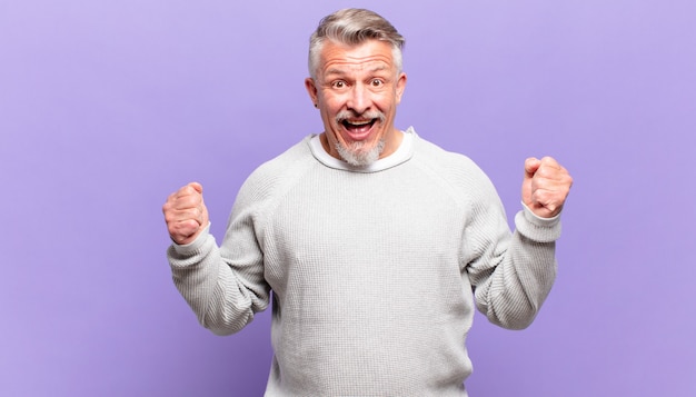 Old senior man feeling shocked, excited and happy, laughing and celebrating success, saying wow!