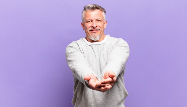 old senior man smiling happily with friendly, confident, positive look, offering and showing an object or concept