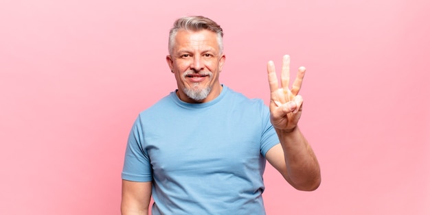 Old senior man smiling and looking friendly, showing number three or third with hand forward, counting down