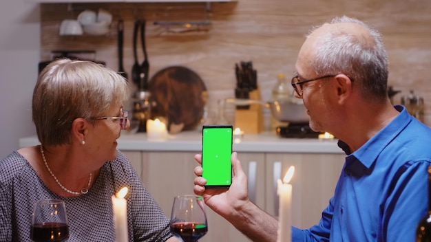 Old senior retired couple holding green screen phone at dinner