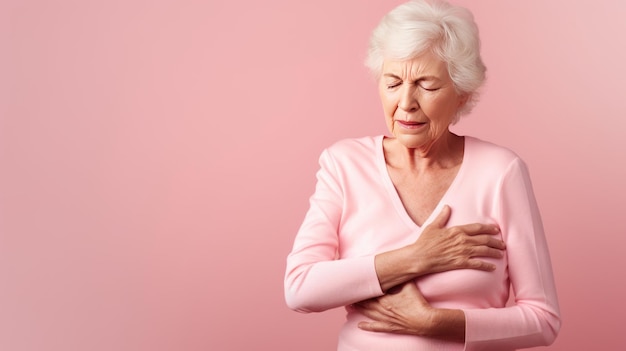 Old Senior Woman presses hand to chest suffers from heart attack unbearable pain isolated on pink