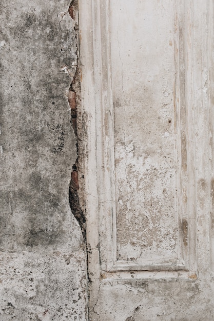 An old shabby pale beige door with gray cement wall with cracks