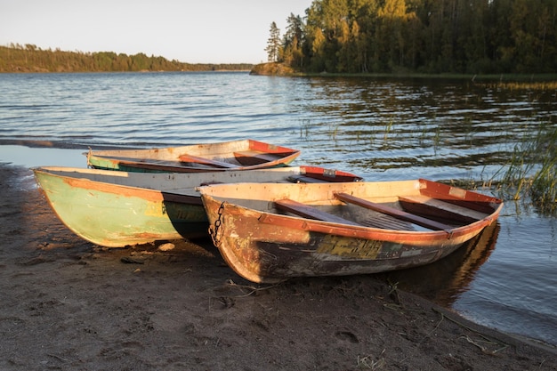 Foto vecchie barche da pesca di legno colorate sulla riva del lago durante il tramonto, foresta d'autunno sullo sfondo