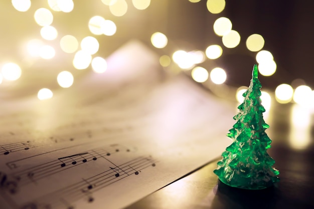 Old sheet with Christmas music notes as background against blurred lights. Christmas music concept