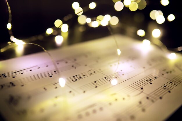 Old sheet with Christmas music notes as background against blurred lights. Christmas music concept