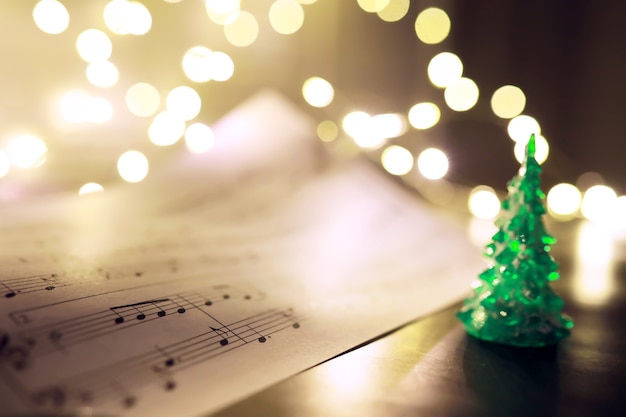 Old sheet with Christmas music notes as background against blurred lights. Christmas music concept