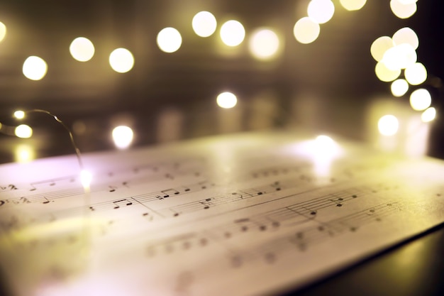 Old sheet with Christmas music notes as background against blurred lights. Christmas music concept