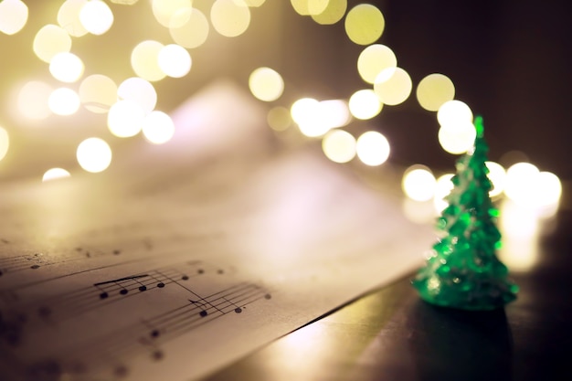 Foto vecchio foglio con note musicali di natale come sfondo contro luci sfocate. concetto di musica di natale